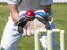 Wicket keeper's gloved hands about to catch a ball as it flies over the stumps.