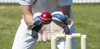 Wicket keeper's gloved hands about to catch a ball as it flies over the stumps.