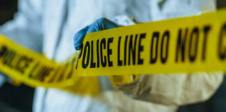 Investigator in white protective suit runs Police tape at scene of investigation