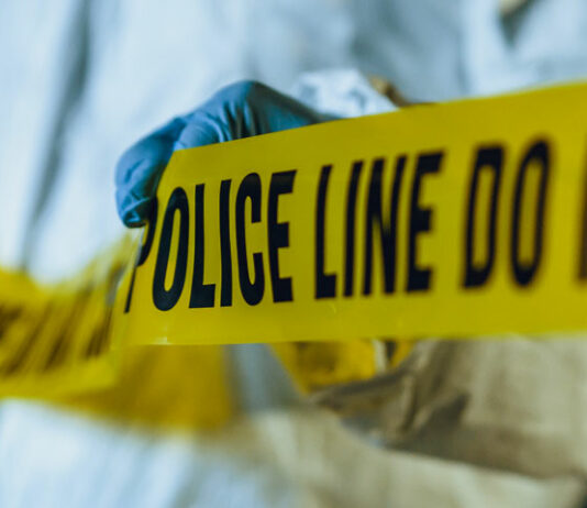 Investigator in white protective suit runs Police tape at scene of investigation