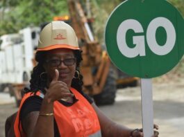 Female road repair worker gives the thumbs up while holding a 'Go' sign.