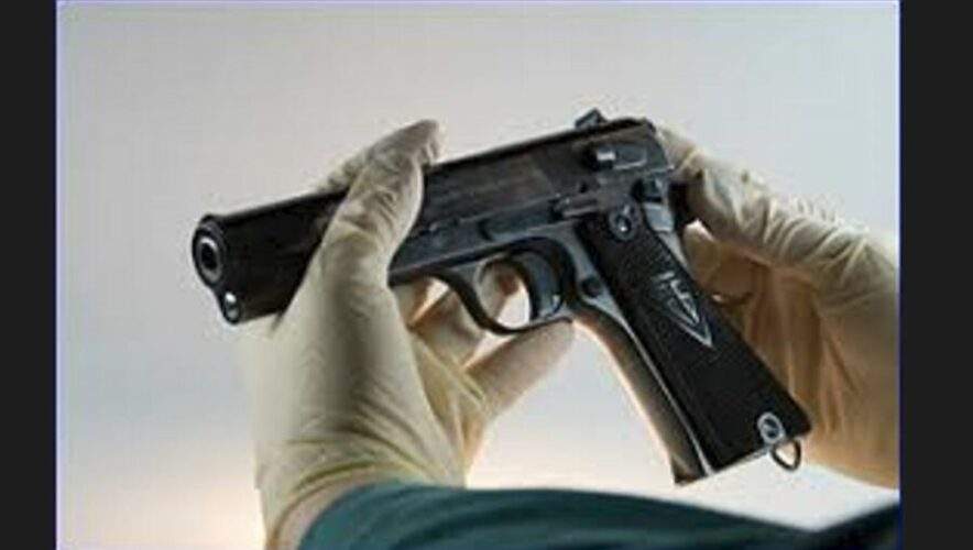 Forensic analyst wearing white gloves examines a pistol.