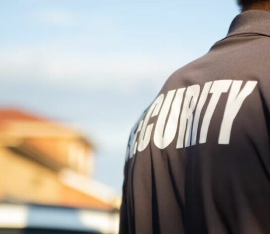 Security guard with back to camera wearing polo shirt marked 'Security'.