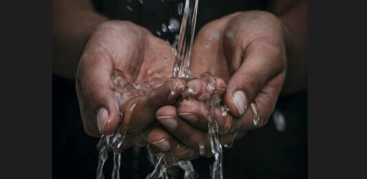 Two hands cupped and water flowing into them from a pipe.