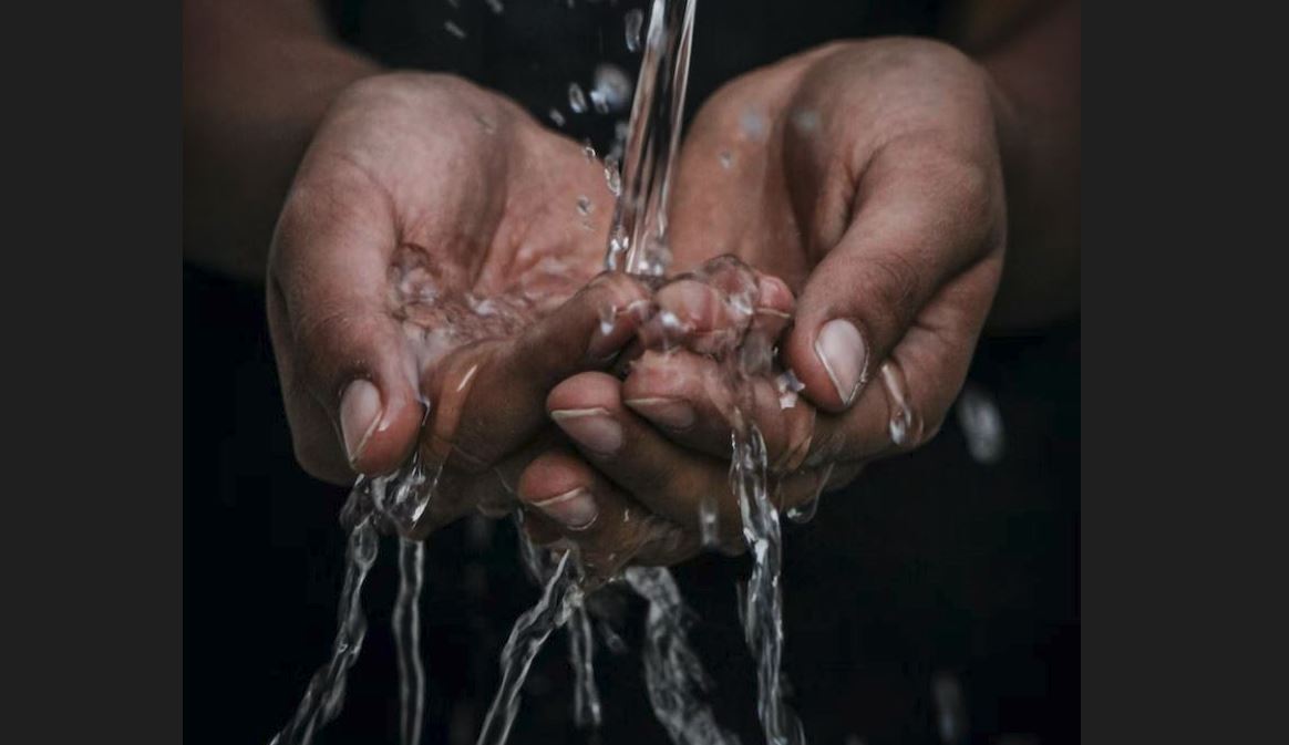 Two hands cupped and water flowing into them from a pipe.