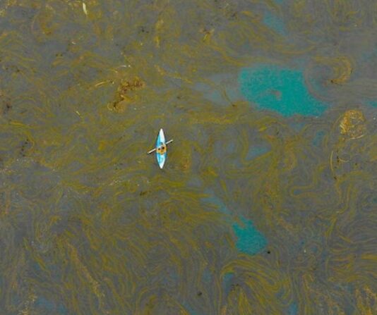 Small boat floating on ocean polluted by oil slick.