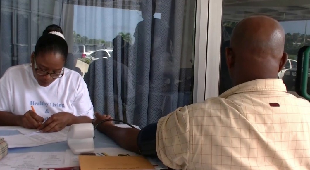 Female medical practitioner writes on a note pad as she takes the blood pressure of a male Soufriere resident.
