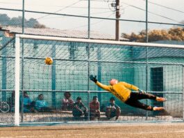 Football goalkeeper lunging to prevent ball entering goal.