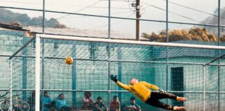 Football goalkeeper lunging to prevent ball entering goal.