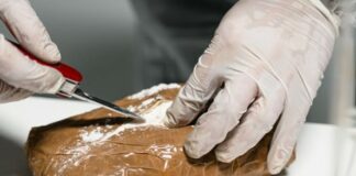 Investigator wearing latex gloves cuts open a package containing cocaine with a penknife.