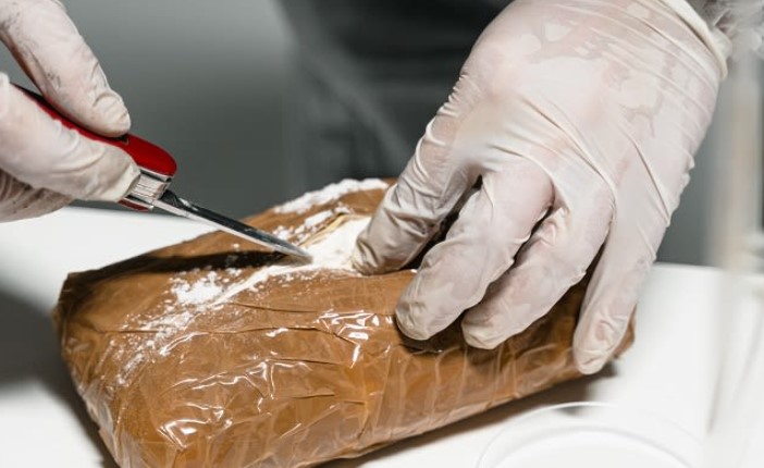 Investigator wearing latex gloves cuts open a package containing cocaine with a penknife.