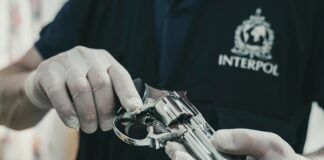 INTERPOL officer wearing latex gloves examines firearm.
