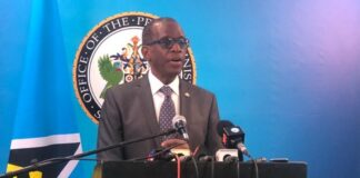 Prime Minister Philip J. Pierre stands at podium addressing reporters at pre-cabinet news briefing.