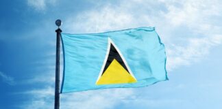 Saint Lucia flag flying against the background of a blue sky with a patch of white cloud.