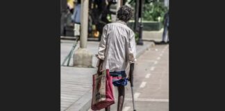Disabled man walking with crutch and bag in left hand.