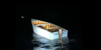 Empty wooden illegal migrant boat with single outboard engine floating on Caribbean sea in the darkness.