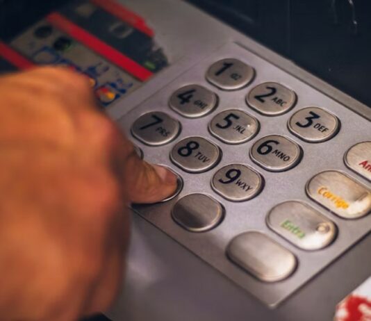 Man's hand punching personal identification number on bank ATM.