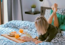 Female tourist on bed with tray containing breakfast.