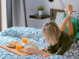 Female tourist on bed with tray containing breakfast.