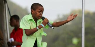 Young calypsonian in school uniform belting out lyrics on stage.