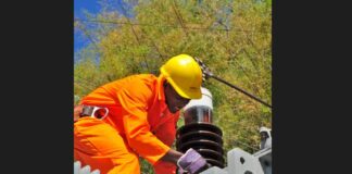 Electricity worker in orange jumpsuit and yellow hardhat at work at an electrical installation.