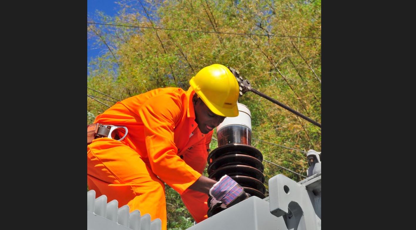 Electricity worker in orange jumpsuit and yellow hardhat at work at an electrical installation.