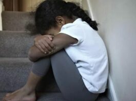 Young girl sits on a step cradling her knees.