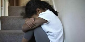 Young girl sits on a step cradling her knees.