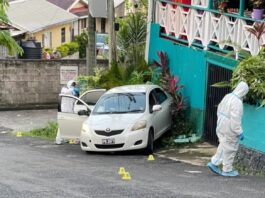 Crime scene investigators in white plastic suits near car in which a man was shot dead in La Clery, Castries.
