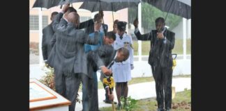 Prime Minister Philip J. Pierre plants a tree amid pouring rain while security detail shelters him with umbrellas.