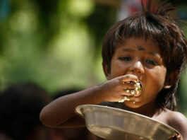 Hungry child eating from a bowl with his hands.