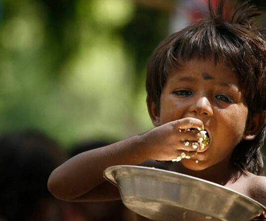 Hungry child eating from a bowl with his hands.