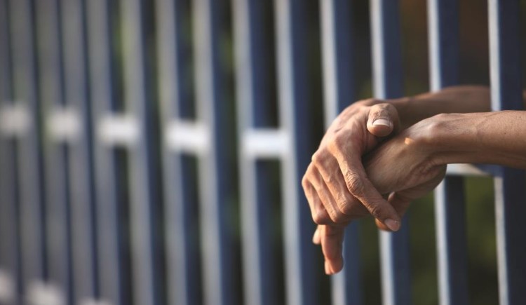 Inmate's hands protrude through prison cell bars.
