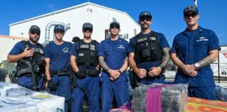 United States Coast Guard personnel pose behind stacks of seized illegal drugs.