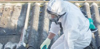 Worker clad in white protective suit inspects asbestos roofing.