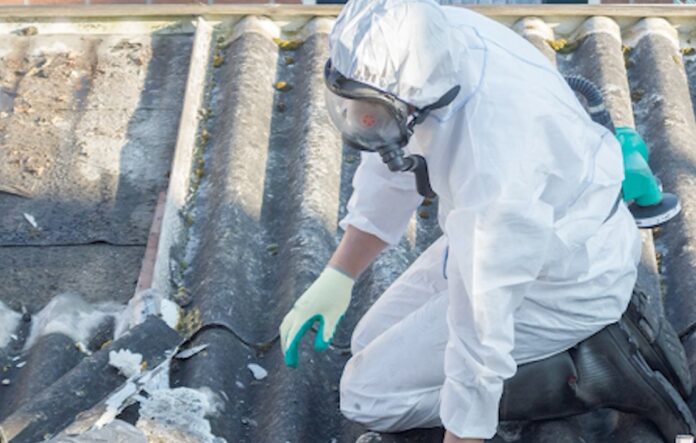 Asbestos roofing Worker clad in white protective suit inspects asbestos roofing.