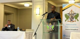 Prime Minister Philip J. Pierre addresses Town Hall meeting in London. Foreign Minister Alva Baptiste sits at the head table.