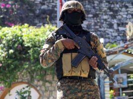 Armed soldier wearing black mask stands guard in Haiti.