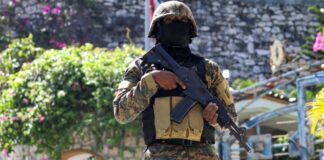 Armed soldier wearing black mask stands guard in Haiti.