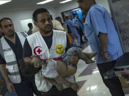 Child injured in Israel-Hamas conflict held in the arms of a Red Crescent official at a field hospital.