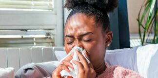 Black woman holds tissue to her nose.