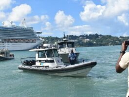 Television cameraman points camera at Marine Police vessel at sea with cruise ship in the background.