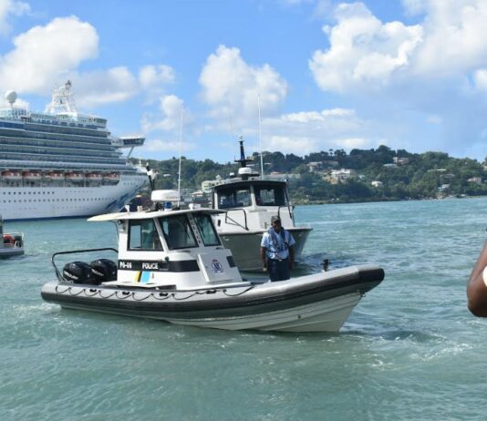 Television cameraman points camera at Marine Police vessel at sea with cruise ship in the background.