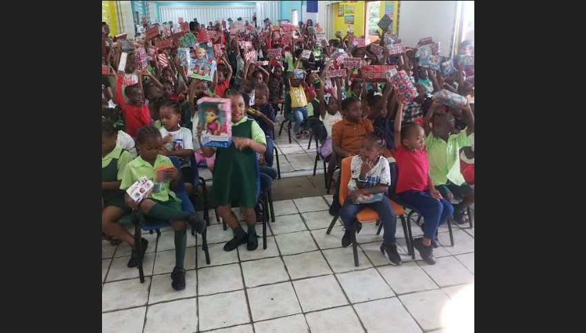 School children in uniform hold up gifts they received from the Sandals Foundation and Hasbro.