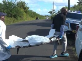 Undertakers in protective suits remove decomposing body on a stretcher towards waiting hearse.