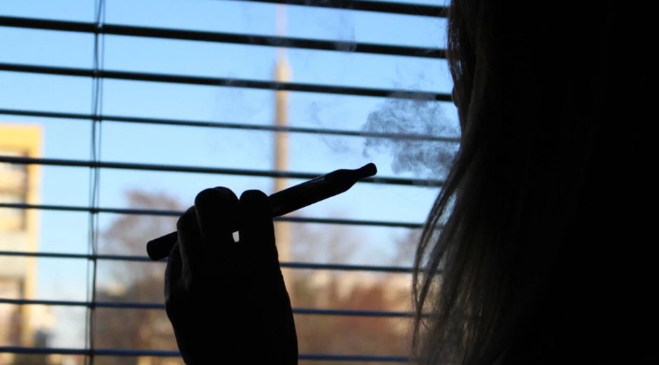 Female in silhouette smoking an e-cigarette near a window.