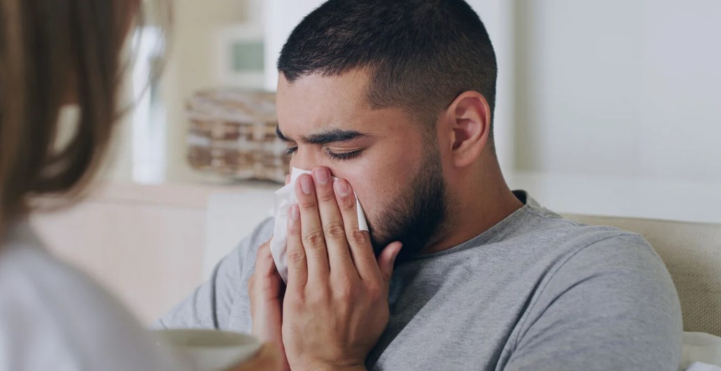 Man covers his nose with a piece of tissue.