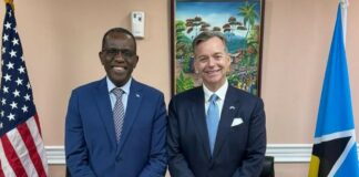 Prime Minister Philip J. Pierre and Ambassador Nyhus stand together in front of the United States and Saint Lucia flags.