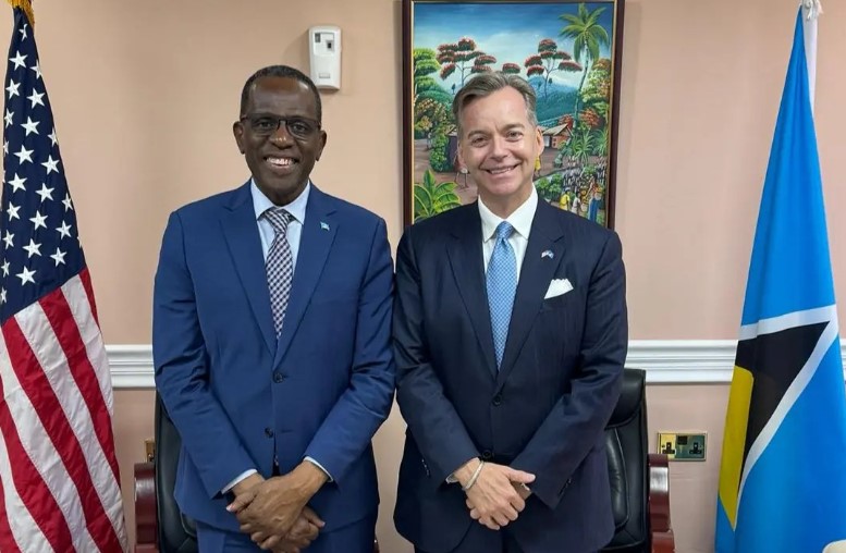 Prime Minister Philip J. Pierre and Ambassador Nyhus stand together in front of the United States and Saint Lucia flags.