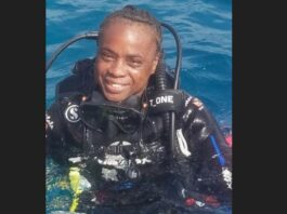 Vanessa Eugene dressed in diving wetsuit with breathing apparatus on her back emerges smiling from the water.